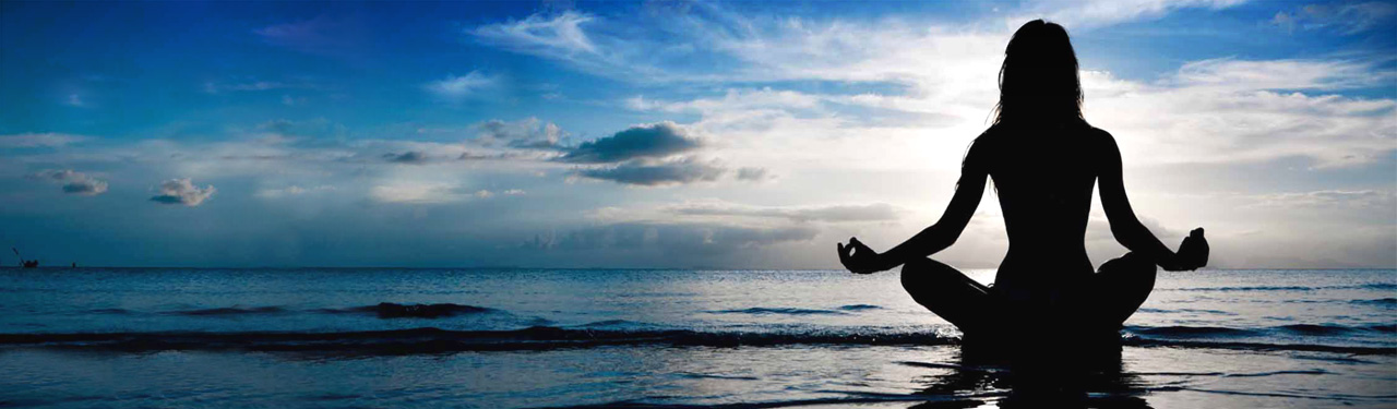 A person seated in meditation beside the sea at sunrise.